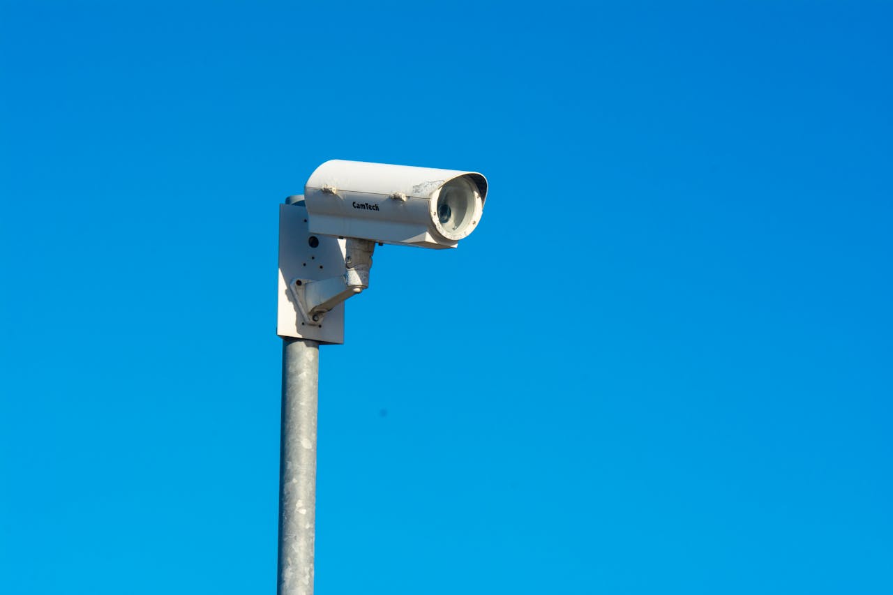 why-choose-us White security camera mounted on a pole under a clear blue sky, symbolizing security and surveillance.